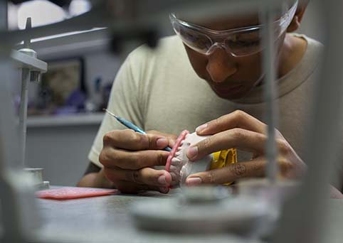 A dental lab technician hand-finishing a custom crown on a tooth model
